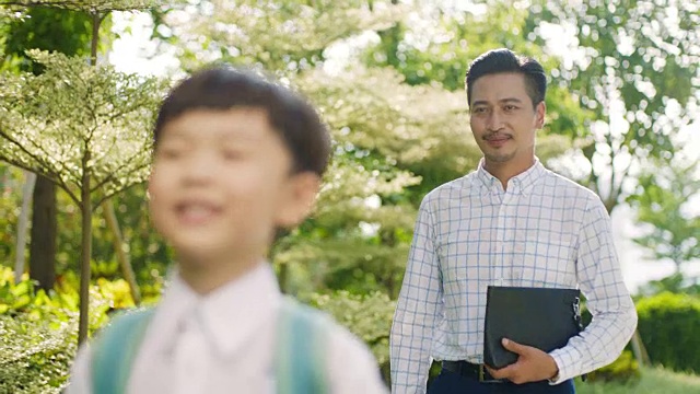 亚洲男孩走过花园与父亲在慢动作照明的学校视频素材