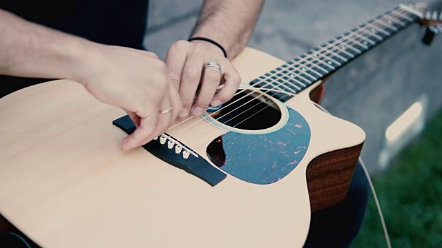 男性的手握着吉他和修理的特写视图。音乐家在改变乐器上的弦视频素材