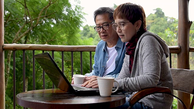 一对老年夫妇一边在阳台上用笔记本电脑聊天视频素材