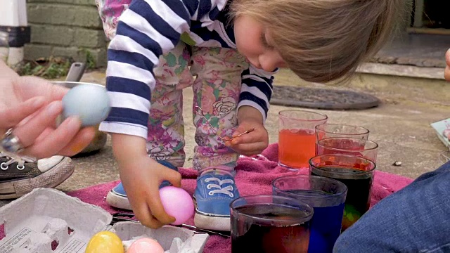可爱的3岁小女孩正在从板条箱中挑选染色的复活节彩蛋视频下载