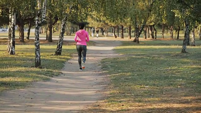 后视图的女运动员在粉色运动服慢跑户外，健康的生活方式的概念。缓慢的运动。视频素材