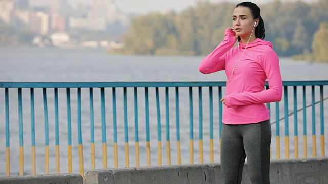 漂亮的女运动员穿着粉红色运动服在户外的一座桥上慢跑，健康的生活方式概念。缓慢的运动。视频下载