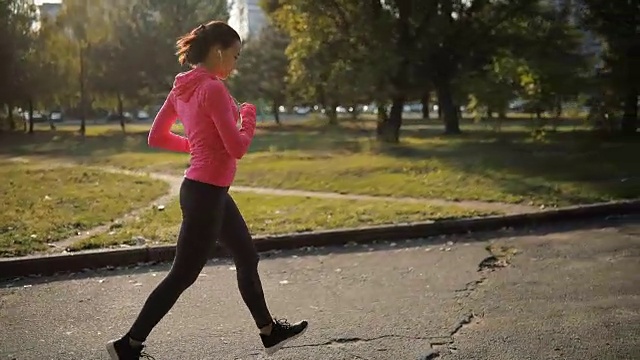 漂亮的女运动员穿着粉红色运动服在户外慢跑，健康的生活方式理念。缓慢的运动。她在用秒表计时。视频素材
