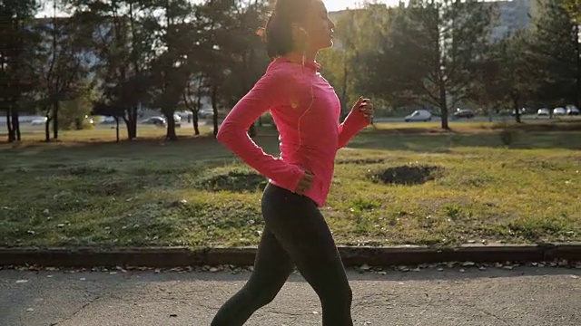 漂亮的女运动员穿着粉红色运动服在户外慢跑，健康的生活方式理念。缓慢的运动。视频素材