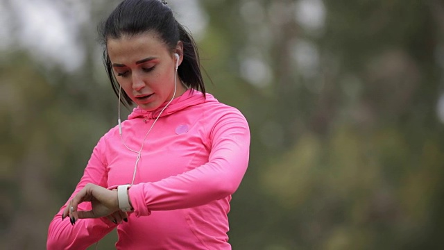 漂亮的女运动员穿着粉红色运动服在户外慢跑，健康的生活方式理念。缓慢的运动。她在用秒表计时。视频素材