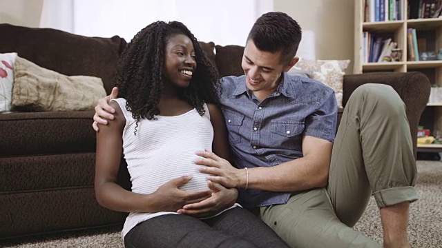 迷人的混血怀孕夫妇坐在地板上，感觉妈妈的肚子视频素材