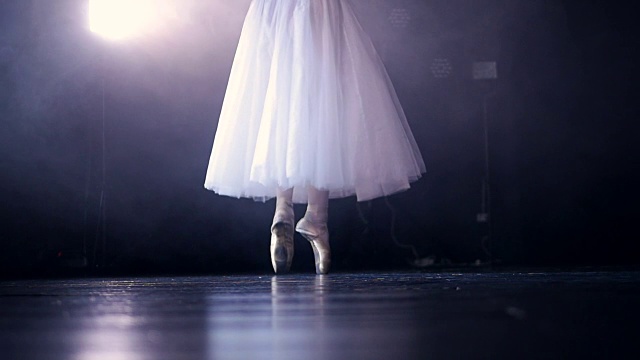白色芭蕾舞演员的腿后面是一个黑色的舞台。视频素材