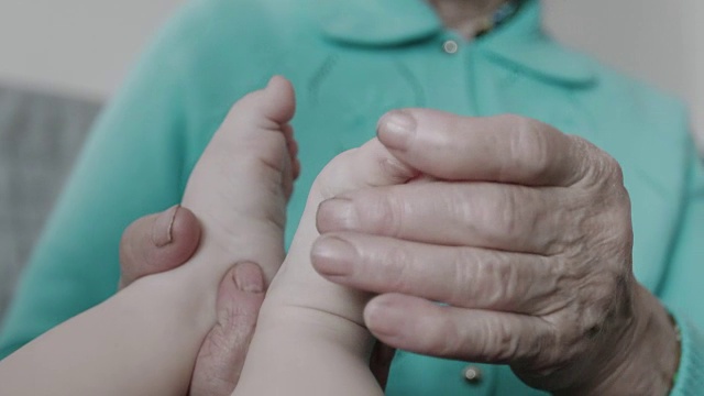 特写祖母抱着新生儿柔软的腿的皱巴巴的手。视频素材