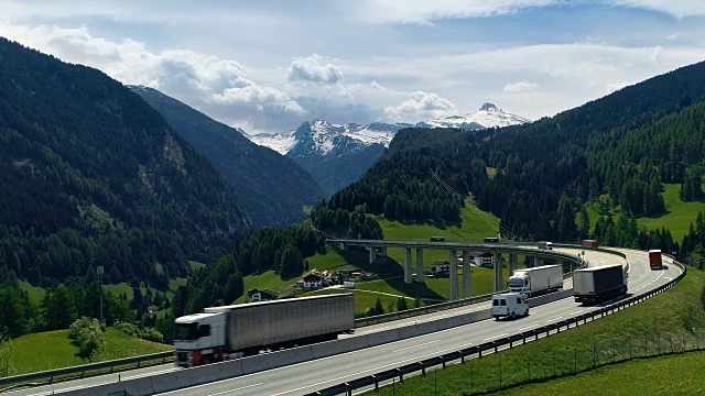 航拍的道路与繁忙的交通延伸到山谷与巨大的山脉与雪峰在背景。视频素材