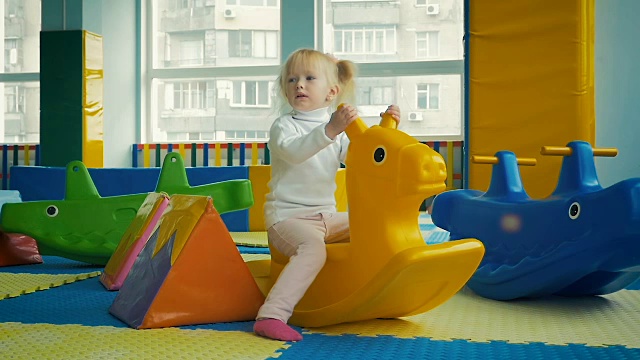 慢镜头:三岁女孩在室内儿童游乐场骑着玩具马。视频素材