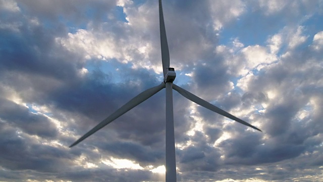 巨大的风力涡轮机在多云的天空下的日落旋转的特写视频素材