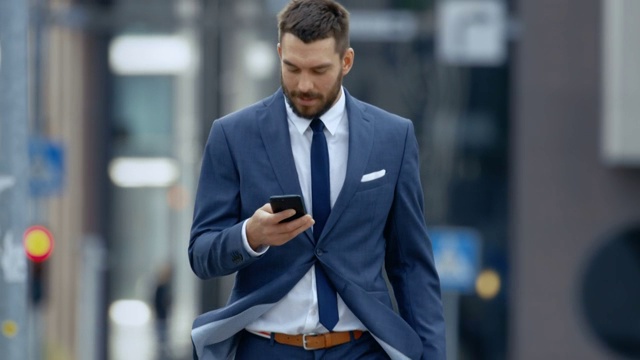一位成功的商人在大城市商业区的街道上使用智能手机。视频素材