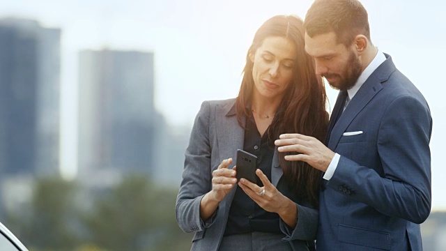 商业男人和商业女人使用智能手机并分享它。以摩天大楼为背景的大城市视频素材