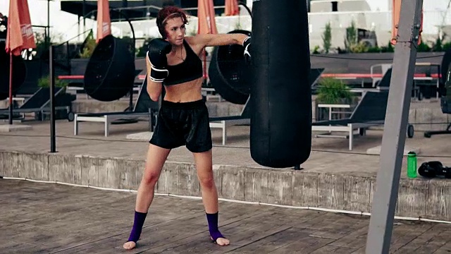 高步伐视频:强壮的运动女拳击手在手套运动与一个包。她用腿打了一个袋子。在外面锻炼。女拳击手训练。Slowmotion拍摄视频素材