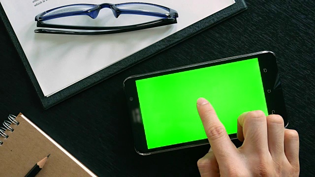 摄影:男用手用手机用绿色屏幕对办公室桌面进行俯视视频素材