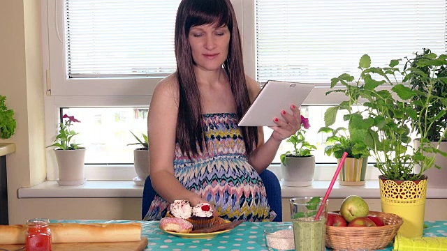孕妇感到饥饿。未来的妈妈用平板电脑吃蛋糕视频素材