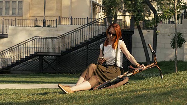 年轻的红发女子骑自行车躺在绿色的草地在城市公园在夏天的一天视频素材