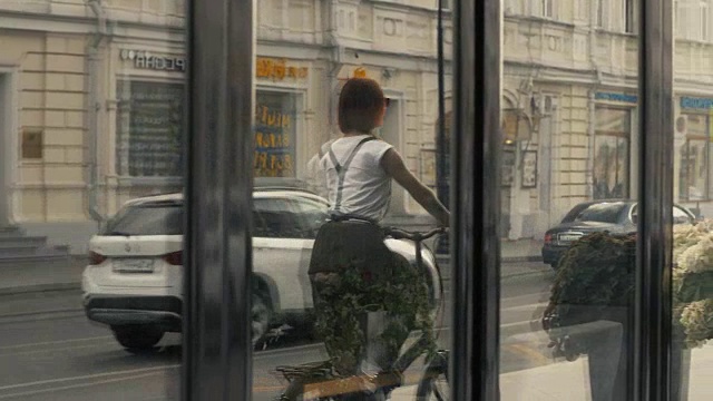 在城市街道上骑着自行车的女子在背景建筑上的倒影视频素材