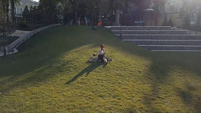 女子骑自行车躺在公园的草地上，使用手机视频素材
