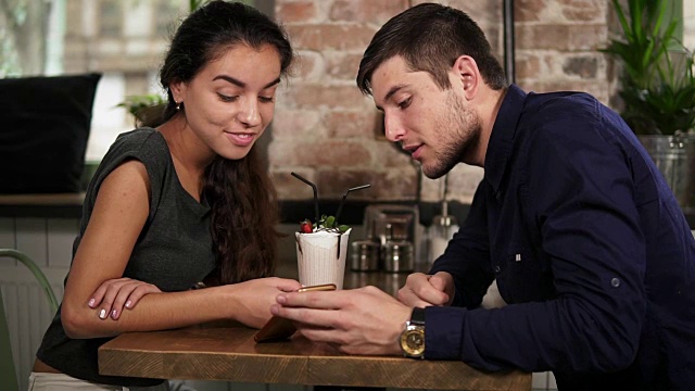 在咖啡店的木桌旁，一对可爱的年轻夫妇手牵着手，打着电话。浪漫的约会视频素材