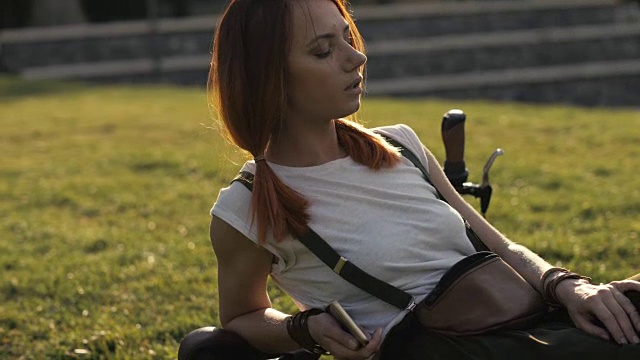 红头发的女人骑自行车休息在夏季公园的绿色草坪上视频素材