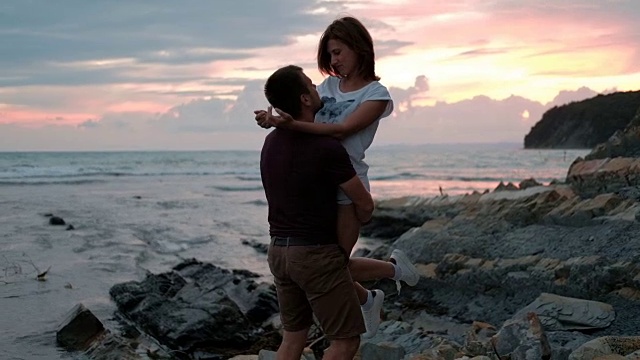 一个年轻人抱着一个女人，站在夏日傍晚的沙滩上视频下载