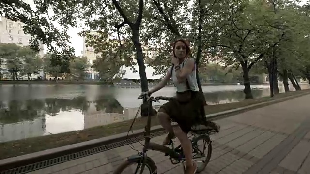 红头发的女人骑着自行车在城市湖泊的背景。女子自行车的城市视频素材