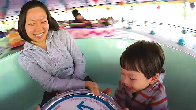 母亲和她的儿子坐在一个转椅杯享受刺激的速度和紧握方向盘在游乐公园的假期。视频下载
