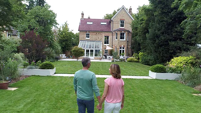 成熟的夫妇手牵着手穿过花园走向屋后视频素材