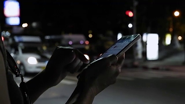 近距离观察女人的手，在她的智能手机上写信息的傍晚道路与汽车灯光的背景。用手机等出租车的女人视频素材
