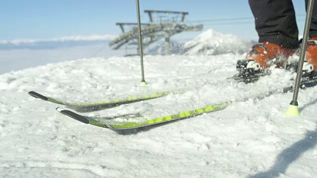慢动作接近:滑雪者在迷雾之上的阳光山上清理滑雪板上的新雪视频素材