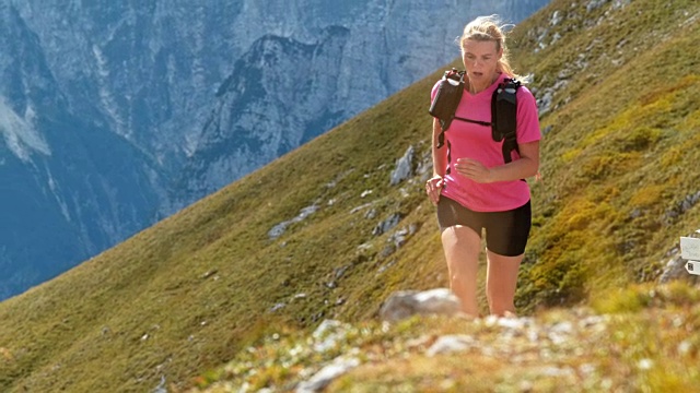 SLO MO女人在阳光下在长满草的山路上跑步视频素材