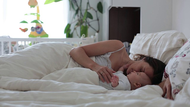 年轻的母亲，在床上抚摸着她刚出生的孩子，把他抱在怀里，幸福的微笑着视频素材