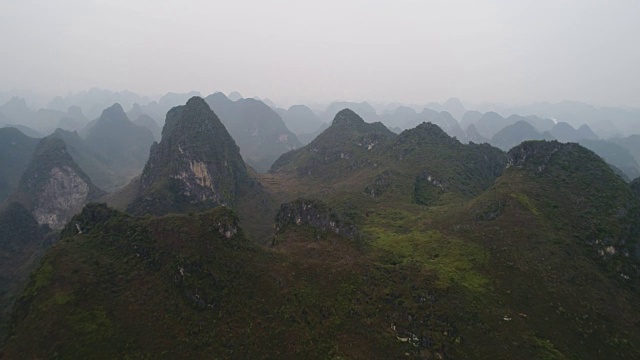 航拍:飞越悬崖和喀斯特丘陵。在中国桂林阳寿县，五颜六色的山被雾或雾霾所覆盖。视频下载