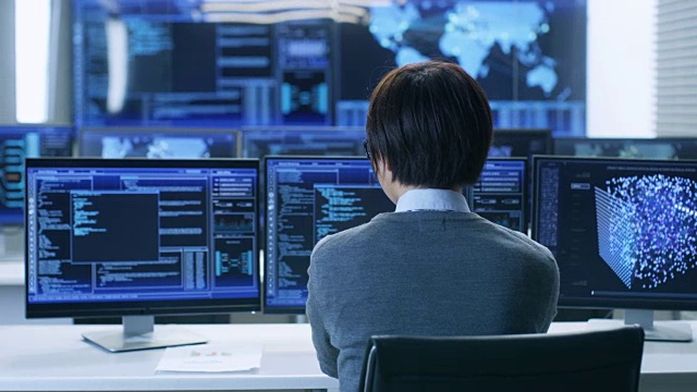 在系统控制室，技术操作员在他的工作站使用多个显示图形的显示器工作。从事人工智能，大数据挖掘，神经网络项目。视频素材