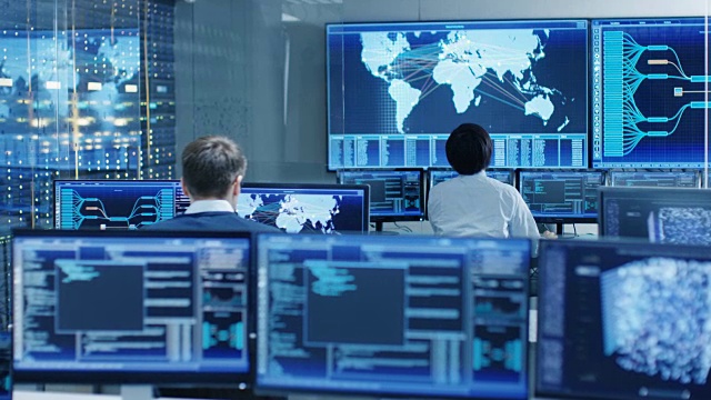 在系统控制室，操作员和管理员坐在他们的工作站，有多个显示图形和物流信息的显示器。视频素材