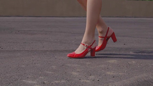 穿着红漆皮凉鞋的漂亮女人走在柏油路上视频下载
