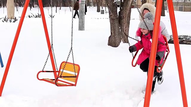 母亲和女儿在冬天霜冻的一天在公园里荡秋千。视频素材
