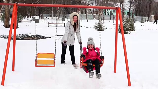 母亲和女儿在冬天霜冻的一天在公园里荡秋千。视频素材