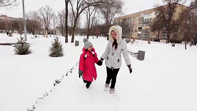 两个女孩，母亲和女儿，在冬天霜冻的一天在公园散步。视频素材