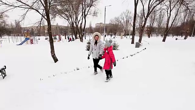 两个女孩，母亲和女儿，在冬天霜冻的一天在公园散步。视频素材