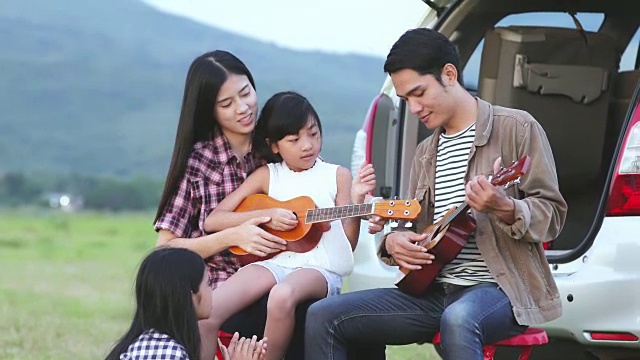 快乐的小女孩和亚洲家庭坐在车里玩尤克里里，享受公路旅行和暑假视频素材