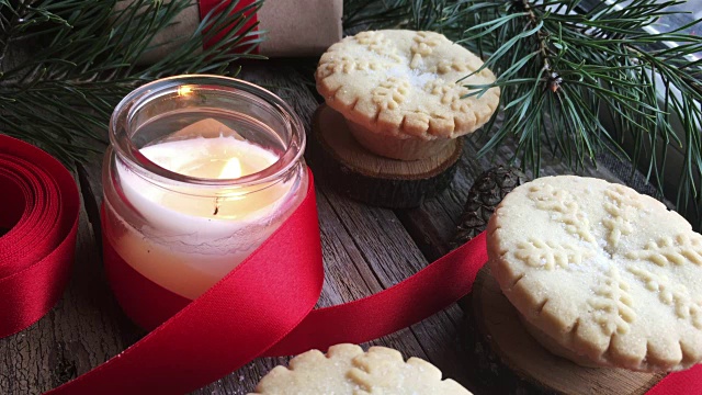 特写燃烧的白色蜡烛和圣诞肉馅饼在质朴的木头桌子上。概念的冬季假期和圣诞烘焙。视频下载