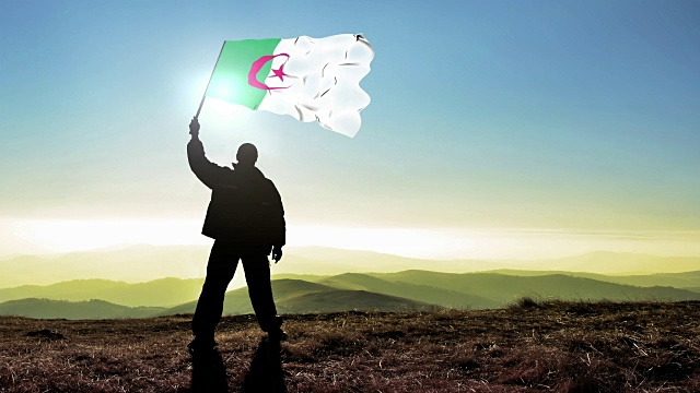 成功的剪影男子冠军挥舞着阿尔及利亚国旗在山顶。Cinemagraph循环背景视频下载