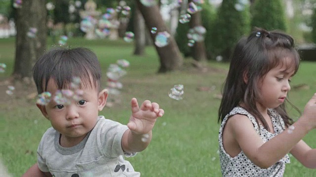 快乐的兄弟姐妹在公园里玩肥皂泡。视频素材
