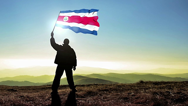 成功的剪影男子冠军在山顶挥舞哥斯达黎加国旗。Cinemagraph循环背景视频下载