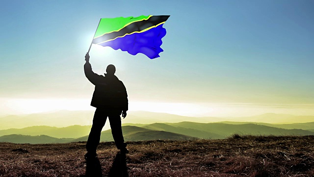 成功剪影男子冠军在山顶挥舞坦桑尼亚国旗，Cinemagraph循环背景视频下载