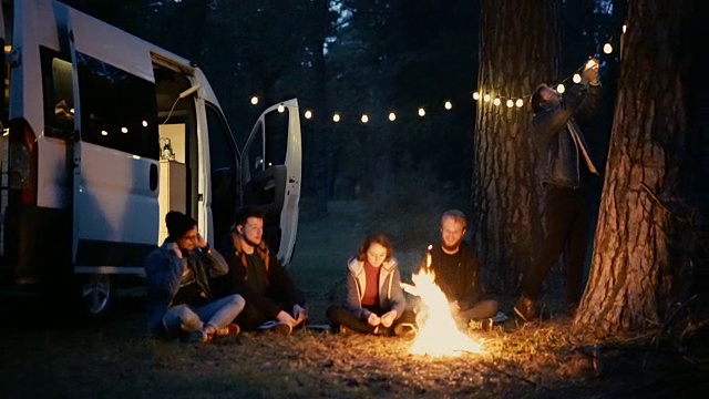 朋友们坐在森林里靠近露营车的篝火旁视频下载