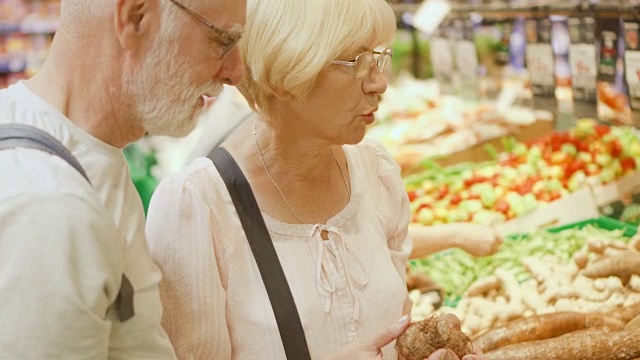 一对老年夫妇在杂货店购物。站在蔬菜部门，选择新鲜的根视频素材