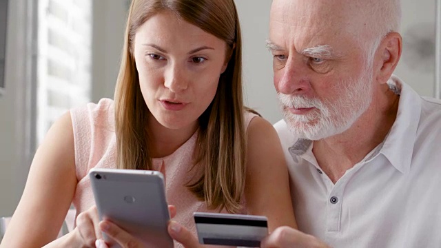老父亲和他的小女儿在家里使用智能手机。用手机刷卡购物视频素材